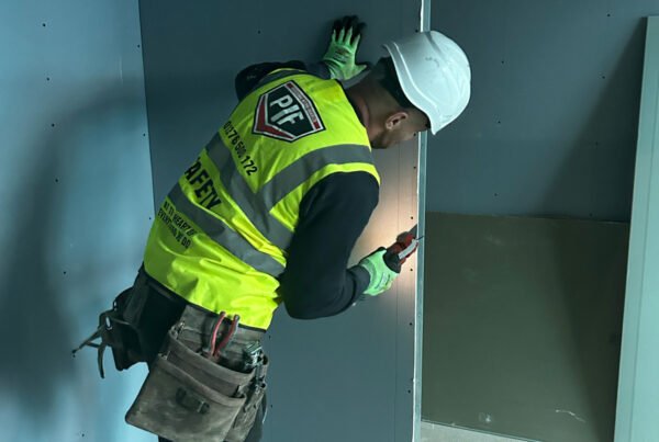 Man in hi-vis drilling dry wall