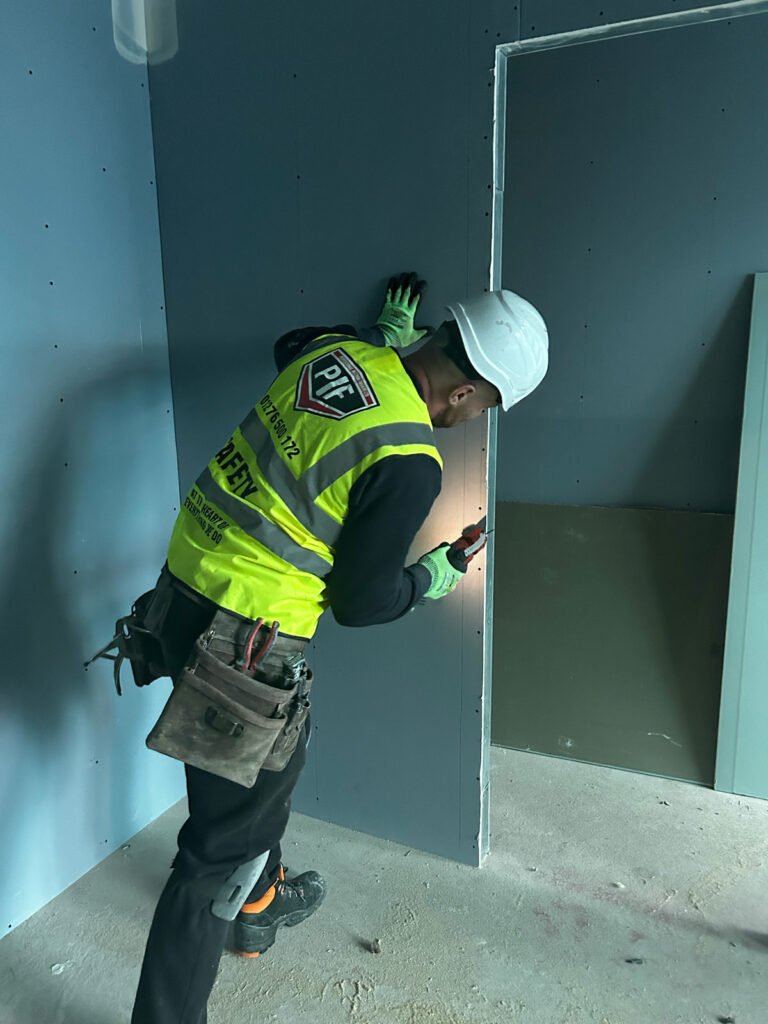 Man in hi-vis drilling dry wall